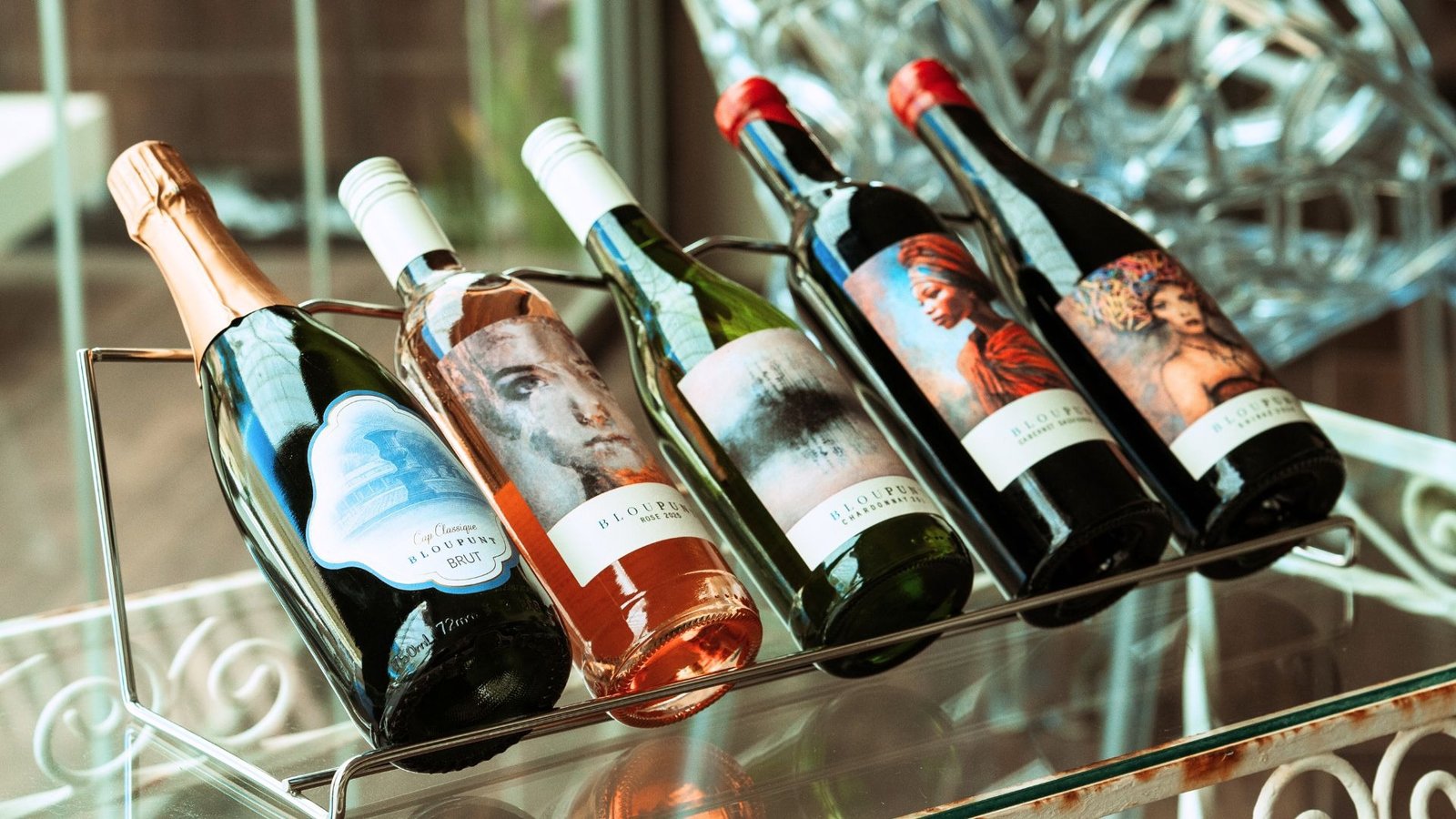 Five Bloupunt wines on a glass table, with Martin and Samantha Lee Osner's art labels