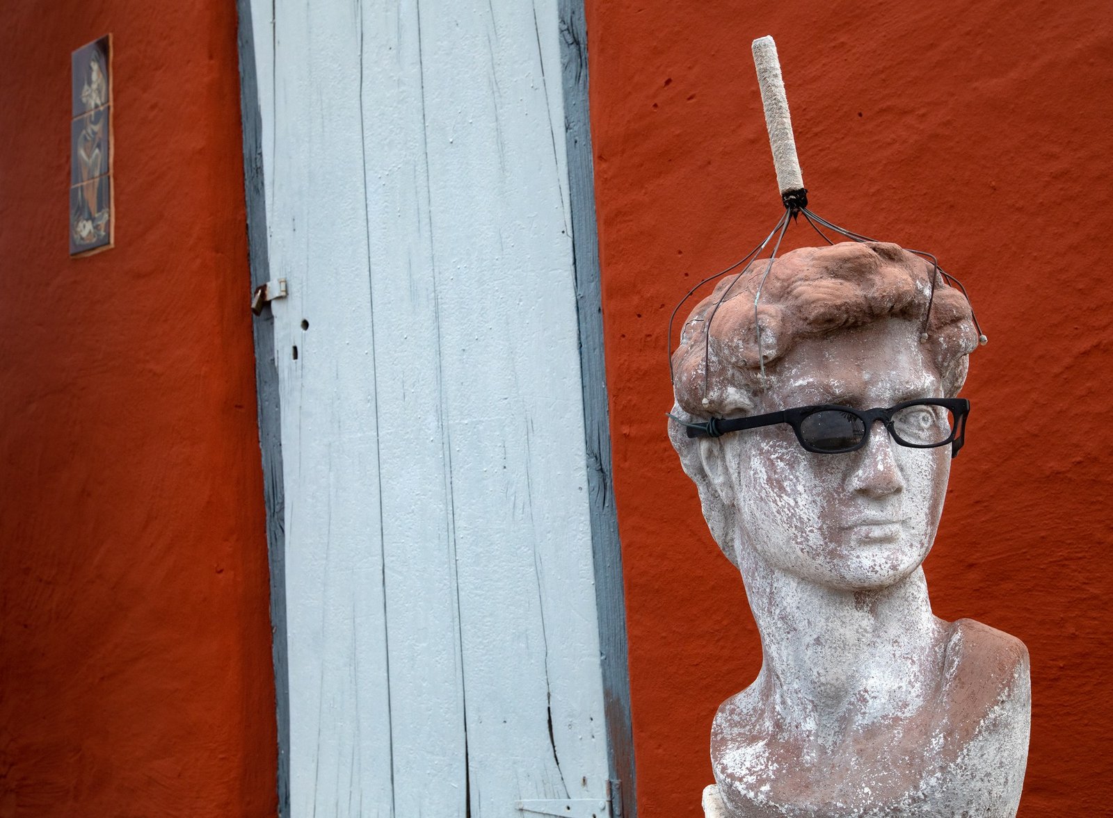 Dawid van die Wolwe by Martin Osner, a David statue in sunglasses and a wire head scratcher against a red wall and a pale blue door