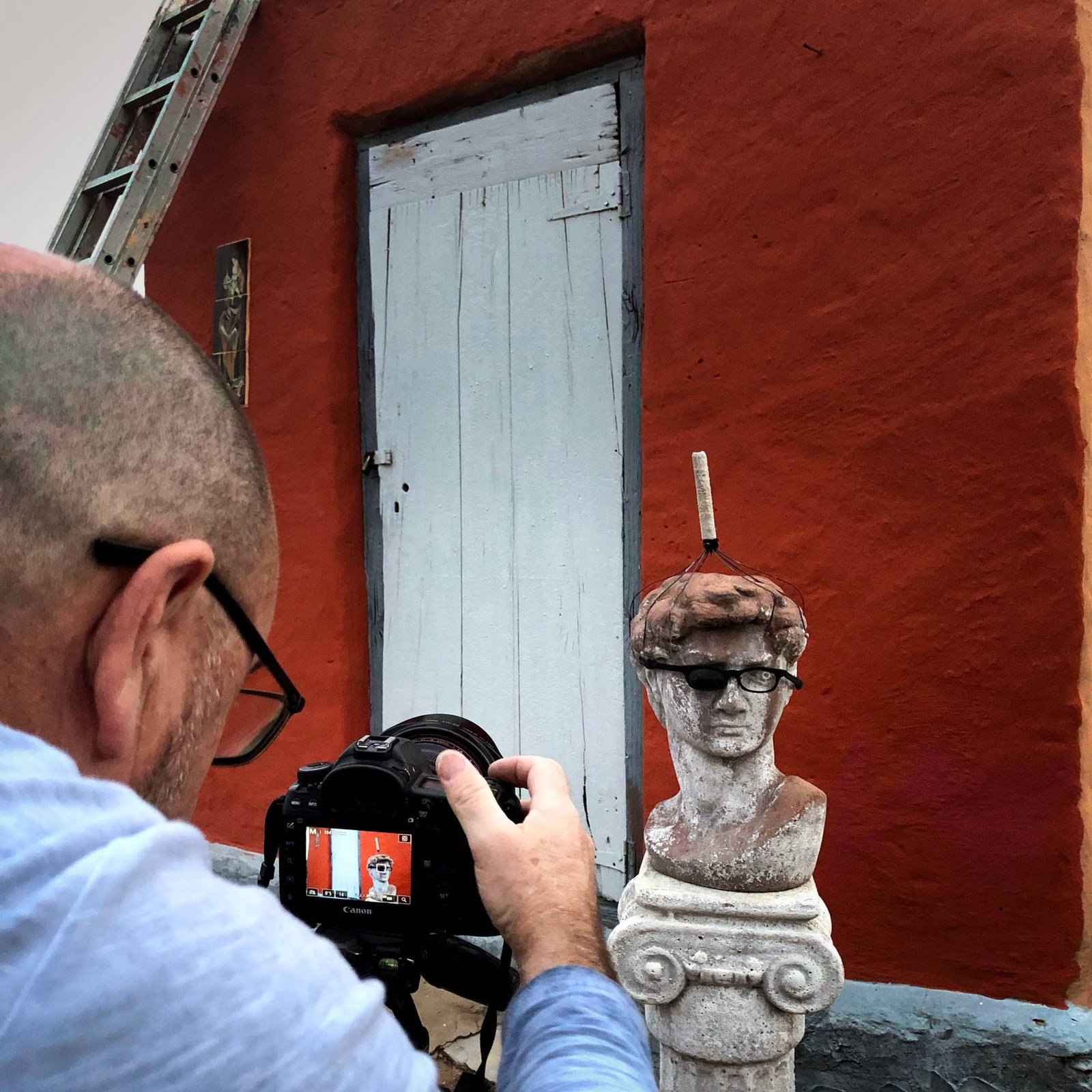 Martin Osner photographing the David statue in sunglasses on its pedestal in front of a red wall in the Karoo