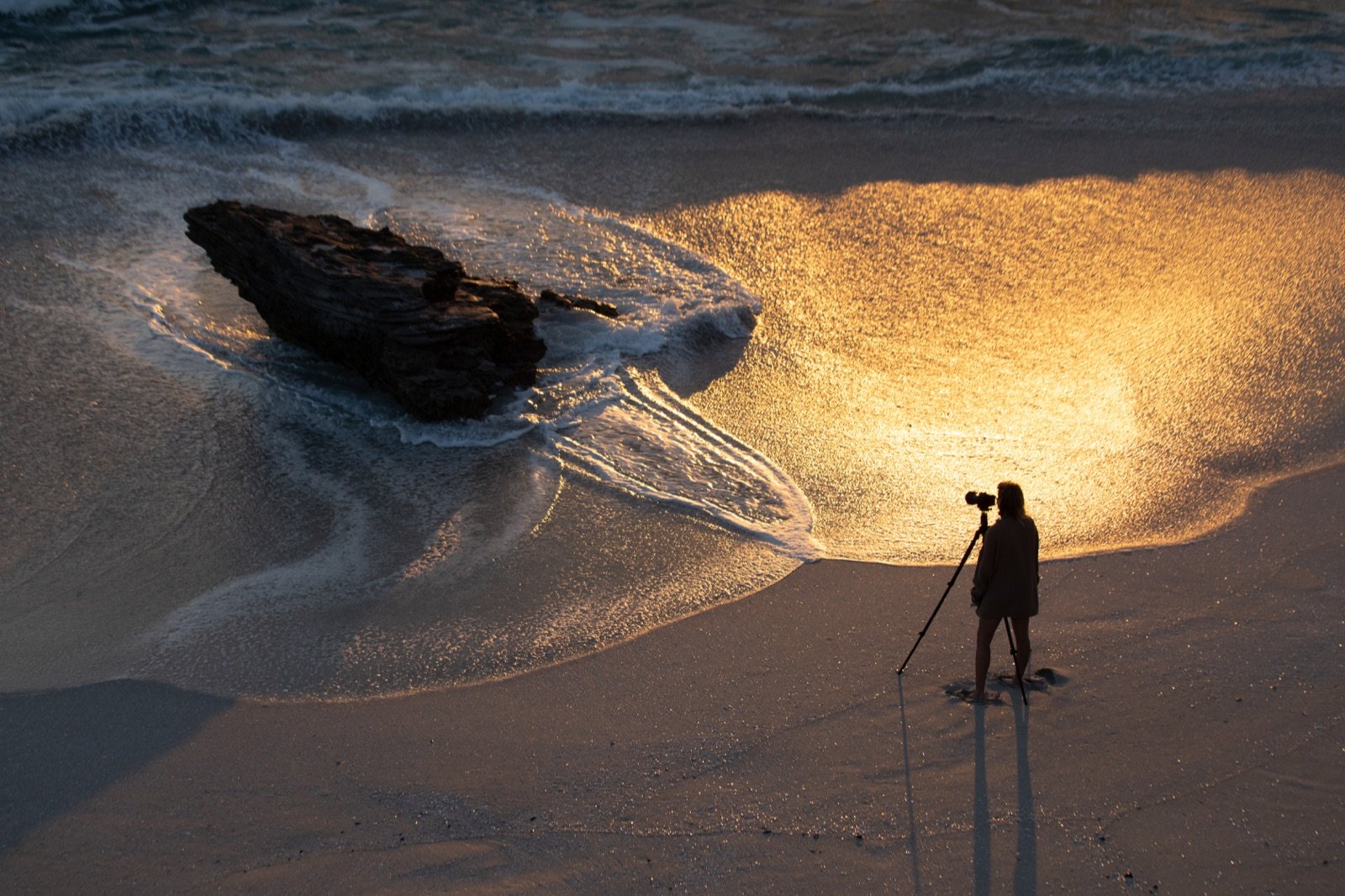 Samantha Lee Osner with her camera on a tripod on a golden beach at sunset